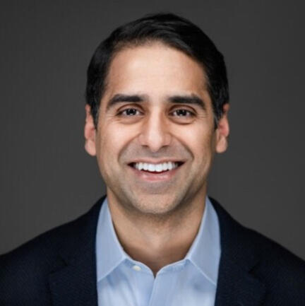 A professional headshot of a smiling Arvin Grover A professional headshot of a smiling Arvin Grover with short dark hair, wearing a dark blazer over a light blue shirt. He is looking directly at the camera with a friendly expression, set against a dark grey background.