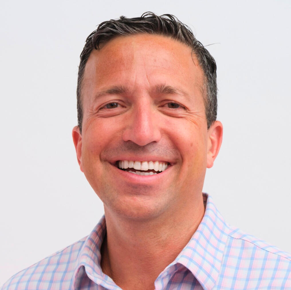 A professional headshot of Alex Mohseni A professional headshot of Alex Mohseni, smiling with short dark hair and wearing a light-colored checkered shirt. He is looking directly at the camera with a friendly expression, set against a clean white background.
